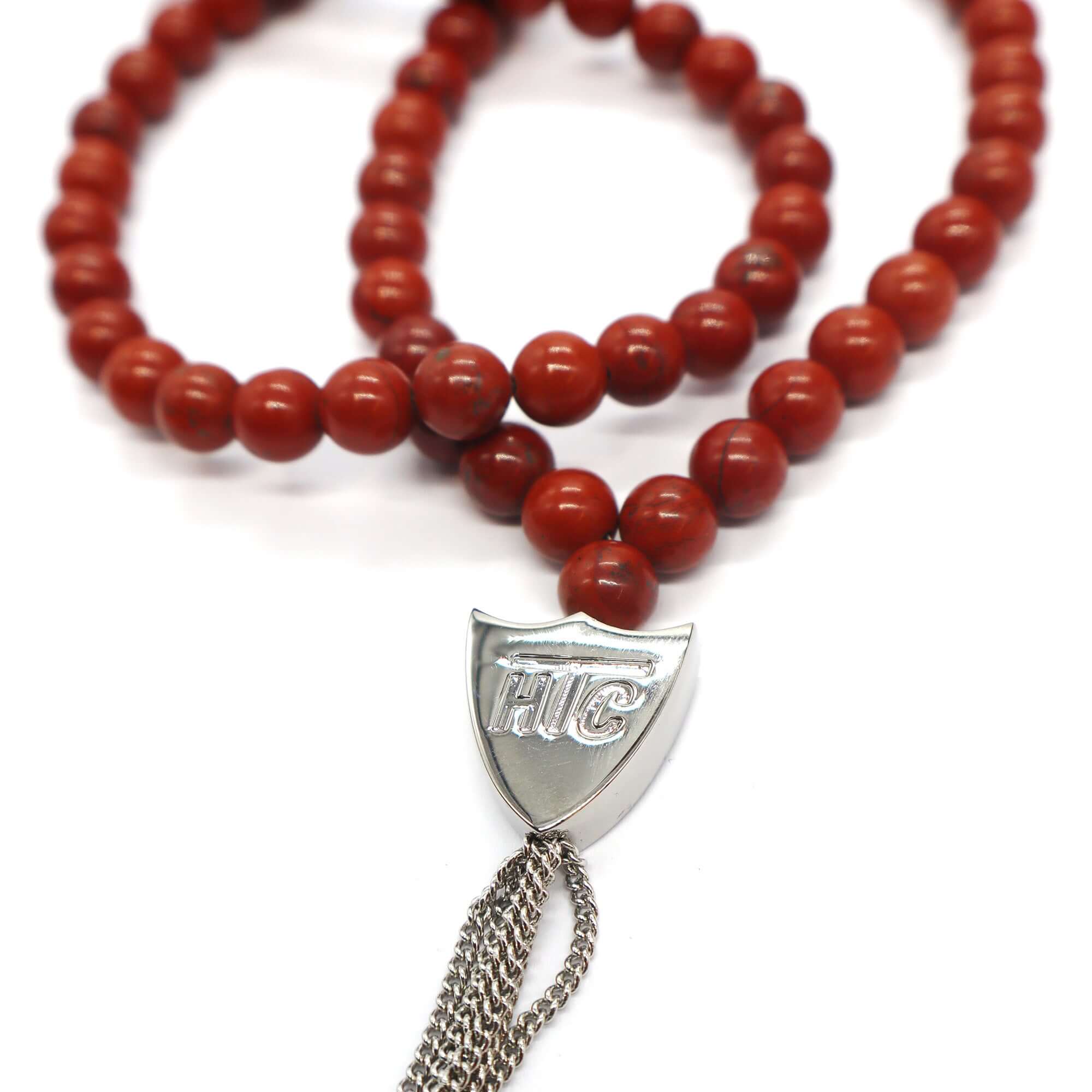 htc los angeles MYSTERY SHIELD NECKLACE RED Red necklace featuring a blend of textile, glass, and metal materials, with a metal HTC logo detail. Hollywood Trading Company