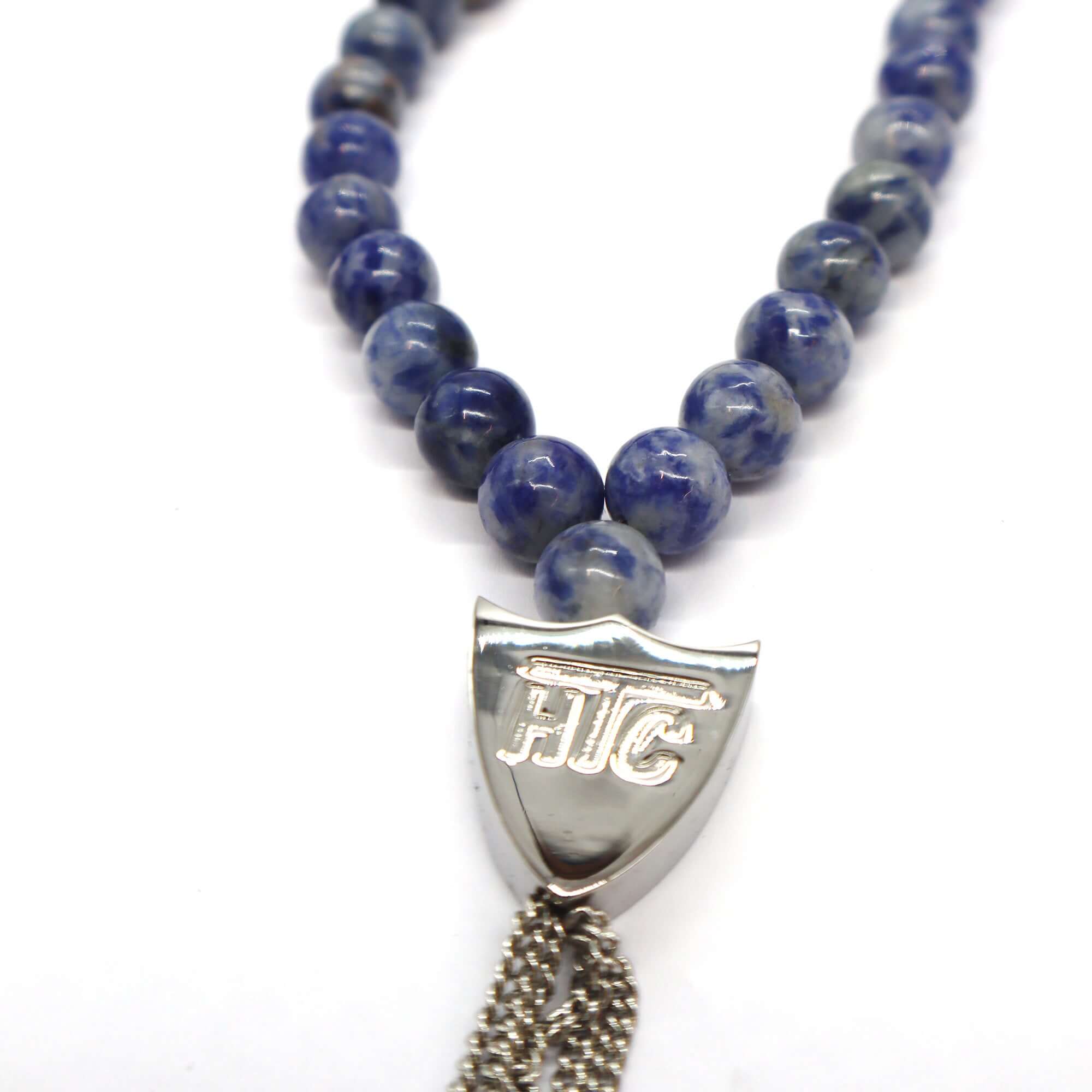 htc los angeles MYSTERY SHIELD NECKLACE SODALITE Sodalite necklace featuring a blend of textile, glass, and metal materials, with a metal HTC logo detail. Hollywood Trading Company