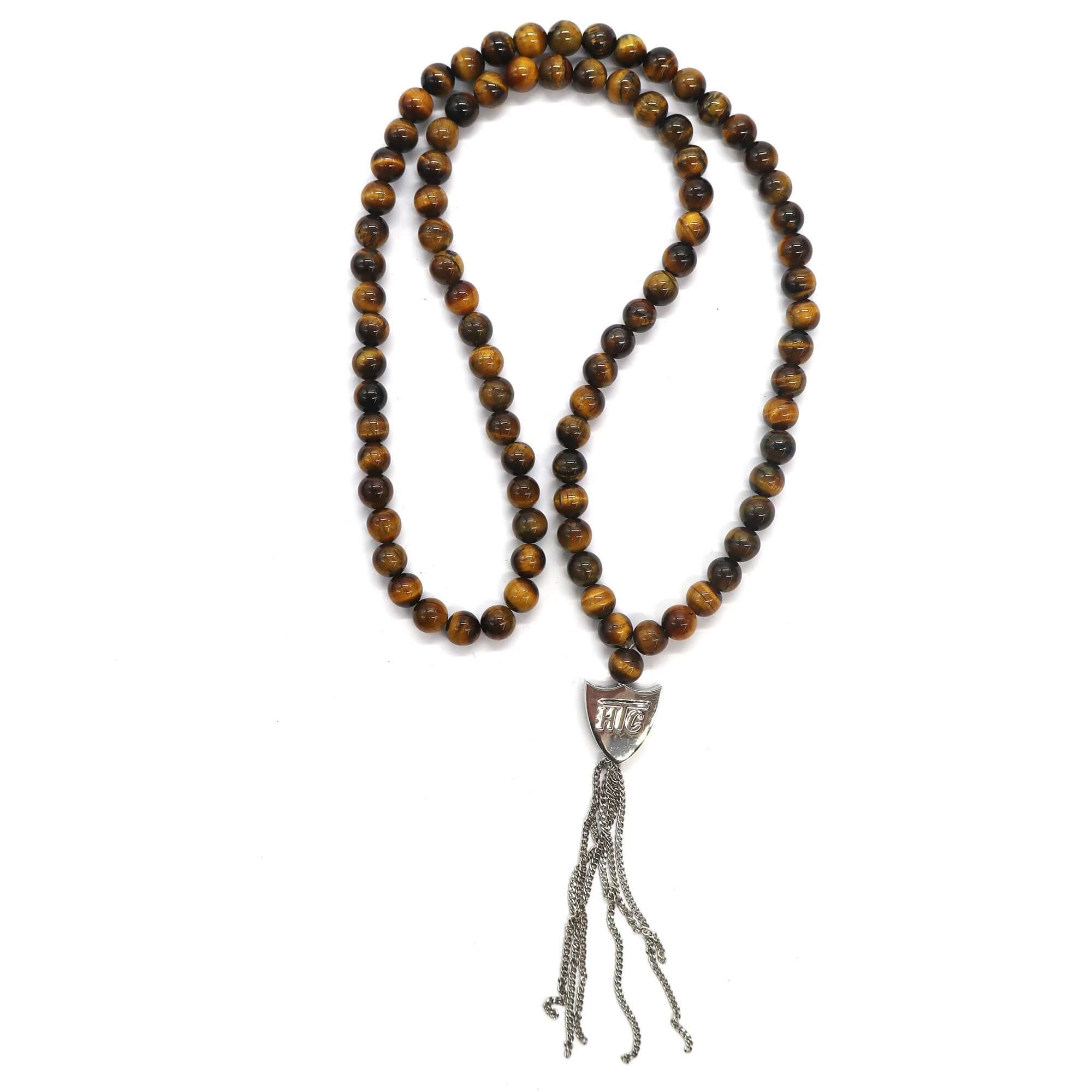 htc los angeles MYSTERY SHIELD NECKLACE TIGER EYE Tiger Eye necklace featuring a blend of textile, glass, and metal materials, with a metal HTC logo detail. Hollywood Trading Company